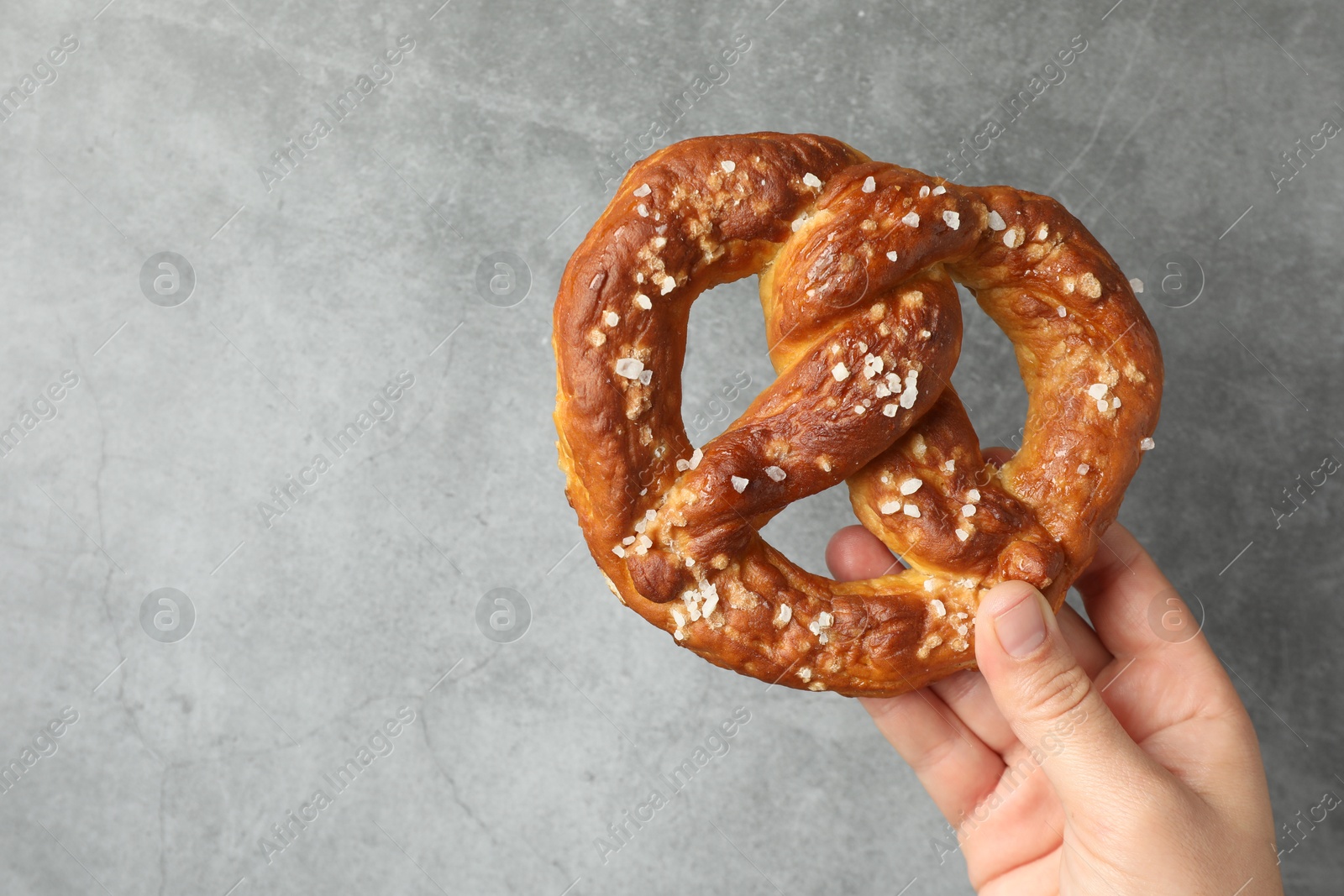 Woman with tasty pretzel near grey textured wall, closeup. Space for text Photo of Woman with tasty pretzel near grey textured wall, closeup. Space for text