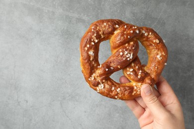 Photo of Woman with tasty pretzel near grey textured wall, closeup. Space for text