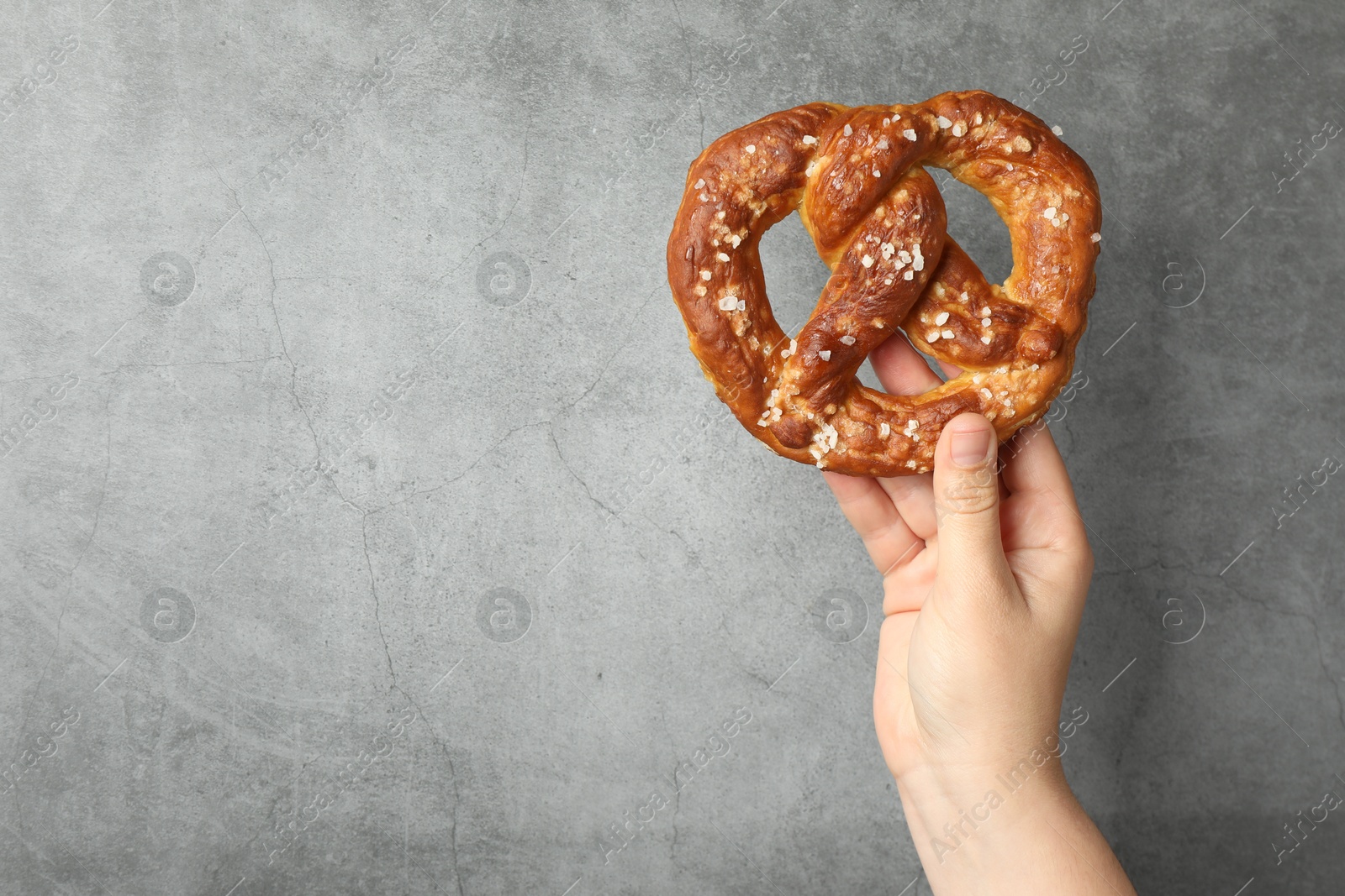 Woman with tasty pretzel near grey textured wall, closeup. Space for text Photo of Woman with tasty pretzel near grey textured wall, closeup. Space for text