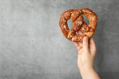 Photo of Woman with tasty pretzel near grey textured wall, closeup. Space for text