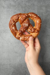 Photo of Woman with tasty pretzel near grey textured wall, closeup