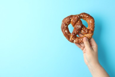 Photo of Woman with tasty pretzel on light blue background, closeup. Space for text