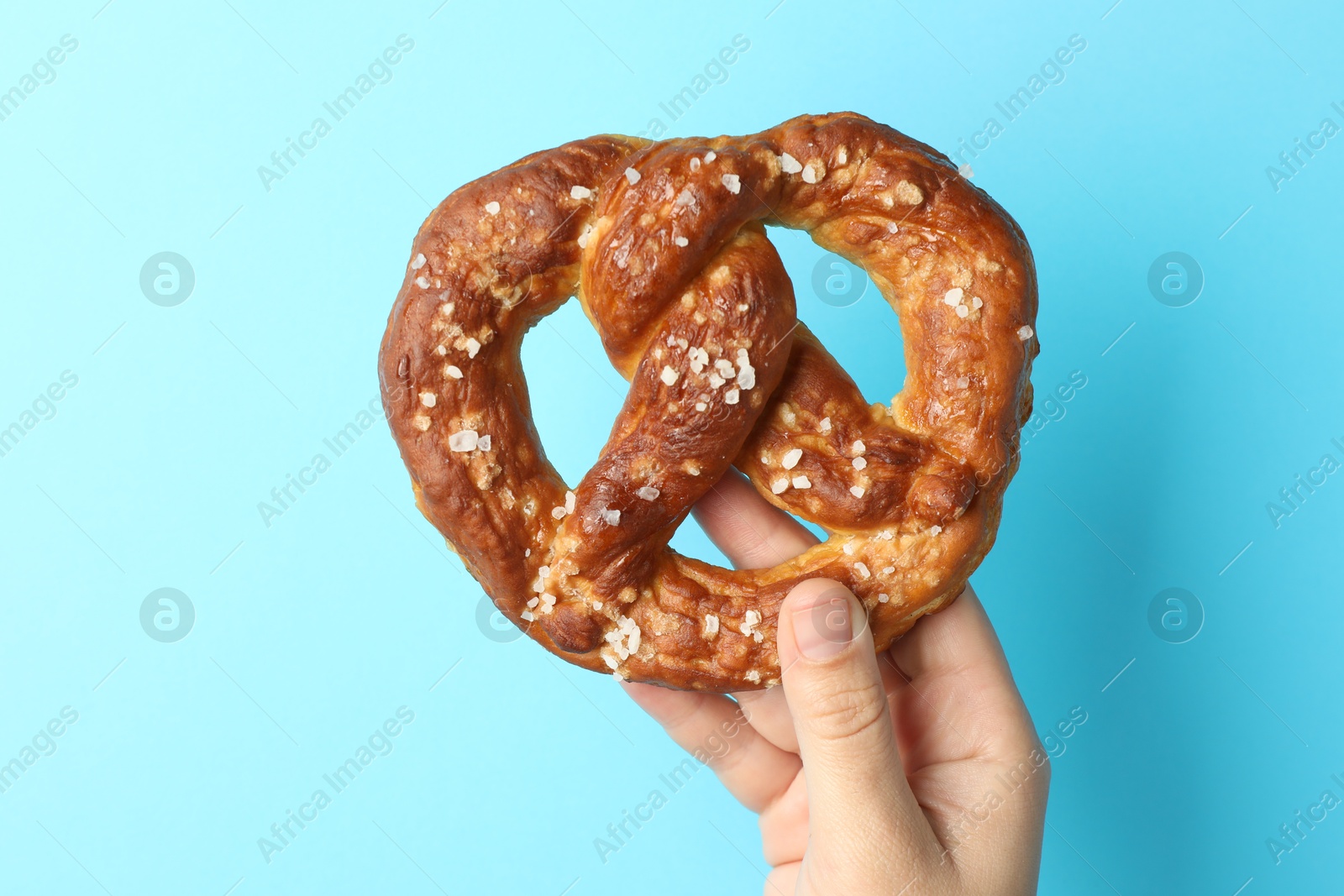 Woman with tasty pretzel on light blue background, closeup Photo of Woman with tasty pretzel on light blue background, closeup