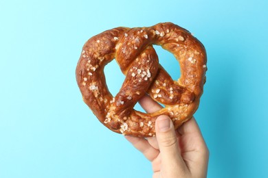 Photo of Woman with tasty pretzel on light blue background, closeup