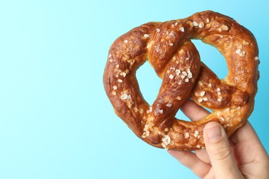 Photo of Woman with tasty pretzel on light blue background, closeup. Space for text