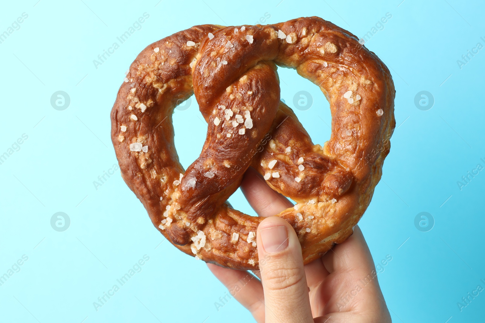 Woman with tasty pretzel on light blue background, closeup Photo of Woman with tasty pretzel on light blue background, closeup