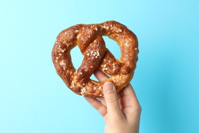 Photo of Woman with tasty pretzel on light blue background, closeup