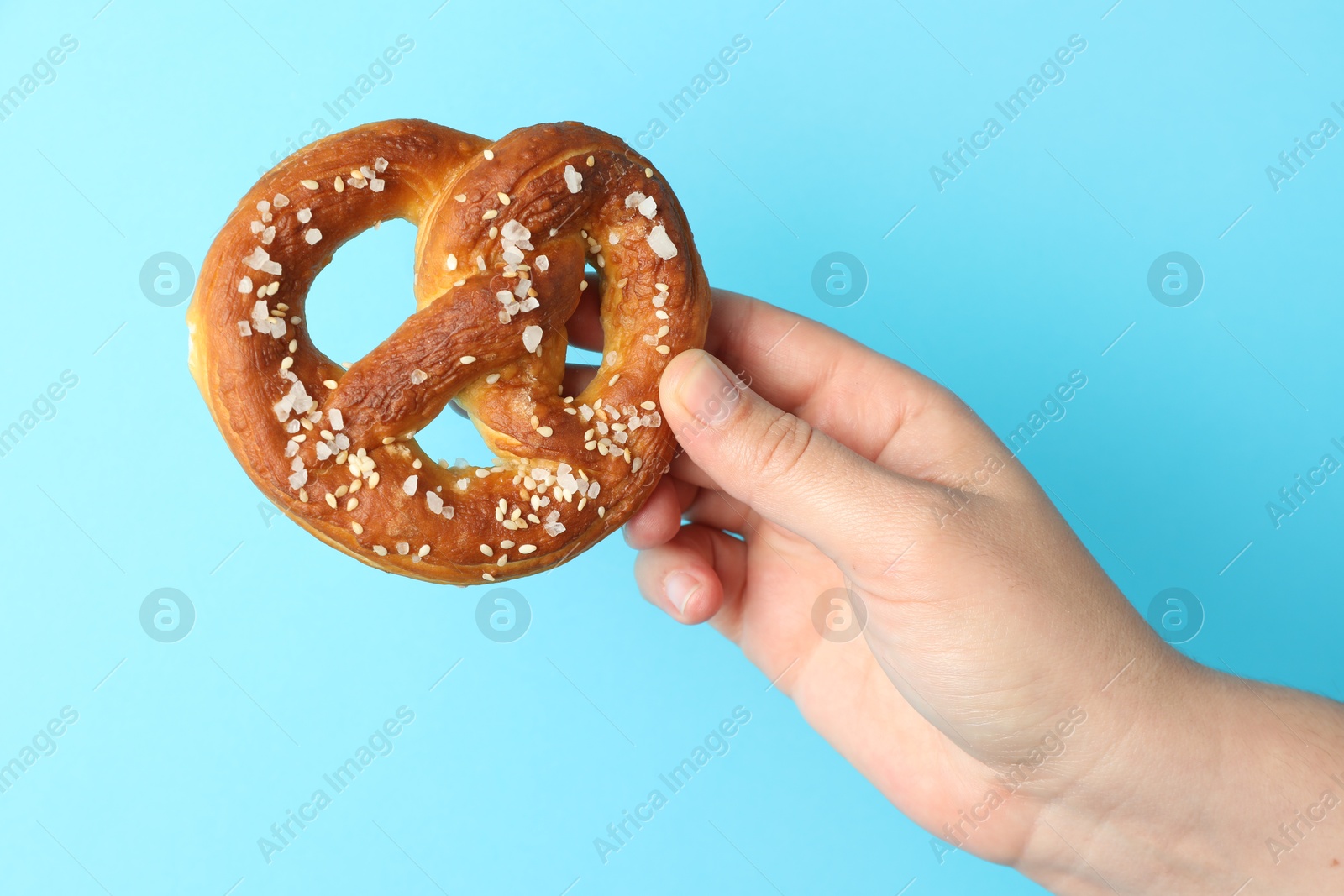 Woman with tasty pretzel on light blue background, closeup Photo of Woman with tasty pretzel on light blue background, closeup