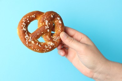 Photo of Woman with tasty pretzel on light blue background, closeup