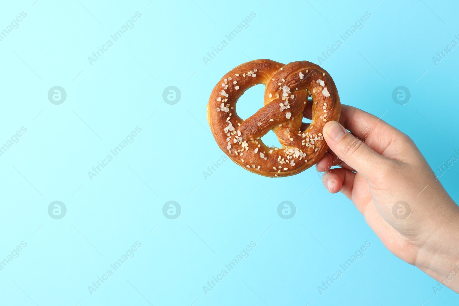 Woman with tasty pretzel on light blue background, closeup. Space for text Photo of Woman with tasty pretzel on light blue background, closeup. Space for text
