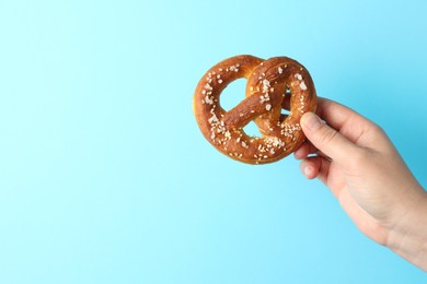 Photo of Woman with tasty pretzel on light blue background, closeup. Space for text