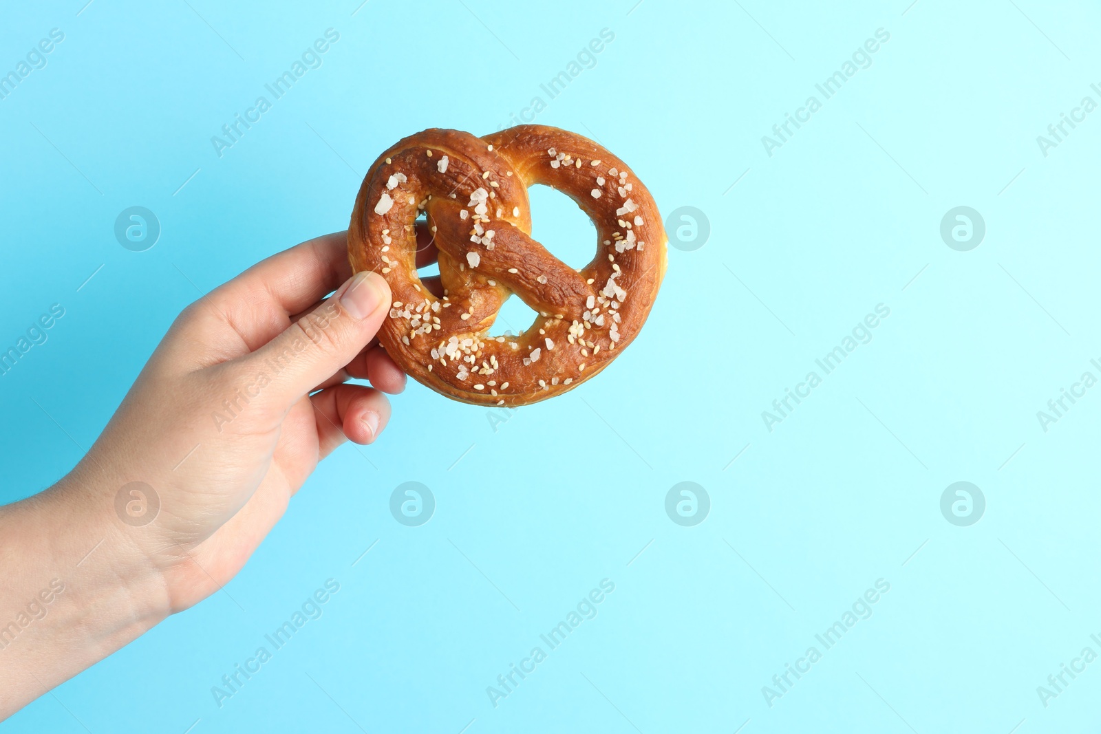 Woman with tasty pretzel on light blue background, closeup. Space for text Photo of Woman with tasty pretzel on light blue background, closeup. Space for text