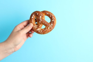 Photo of Woman with tasty pretzel on light blue background, closeup. Space for text