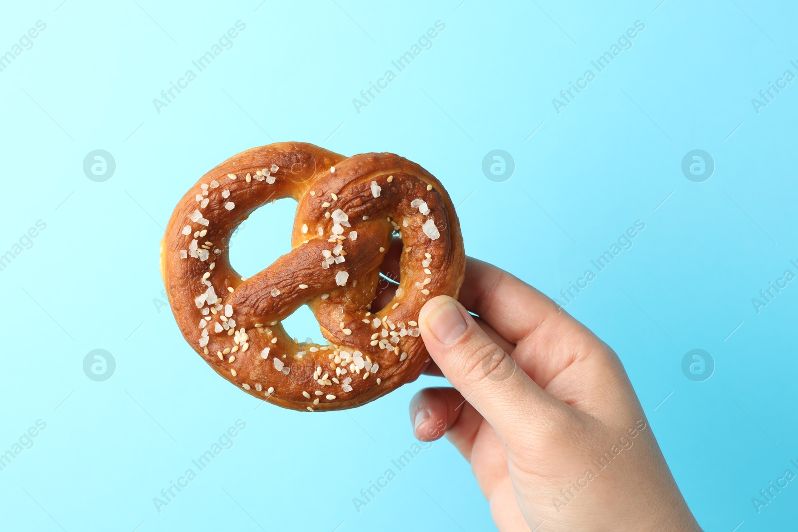 Woman with tasty pretzel on light blue background, closeup Photo of Woman with tasty pretzel on light blue background, closeup