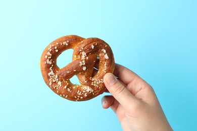 Photo of Woman with tasty pretzel on light blue background, closeup