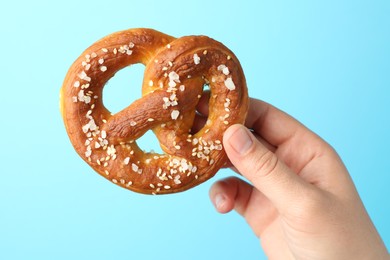 Photo of Woman with tasty pretzel on light blue background, closeup