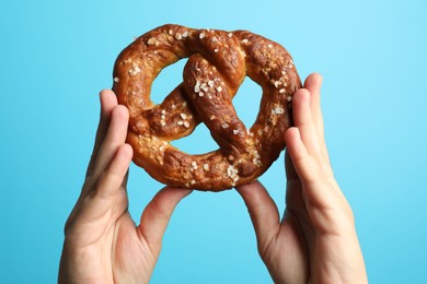 Photo of Woman with tasty pretzel on light blue background, closeup