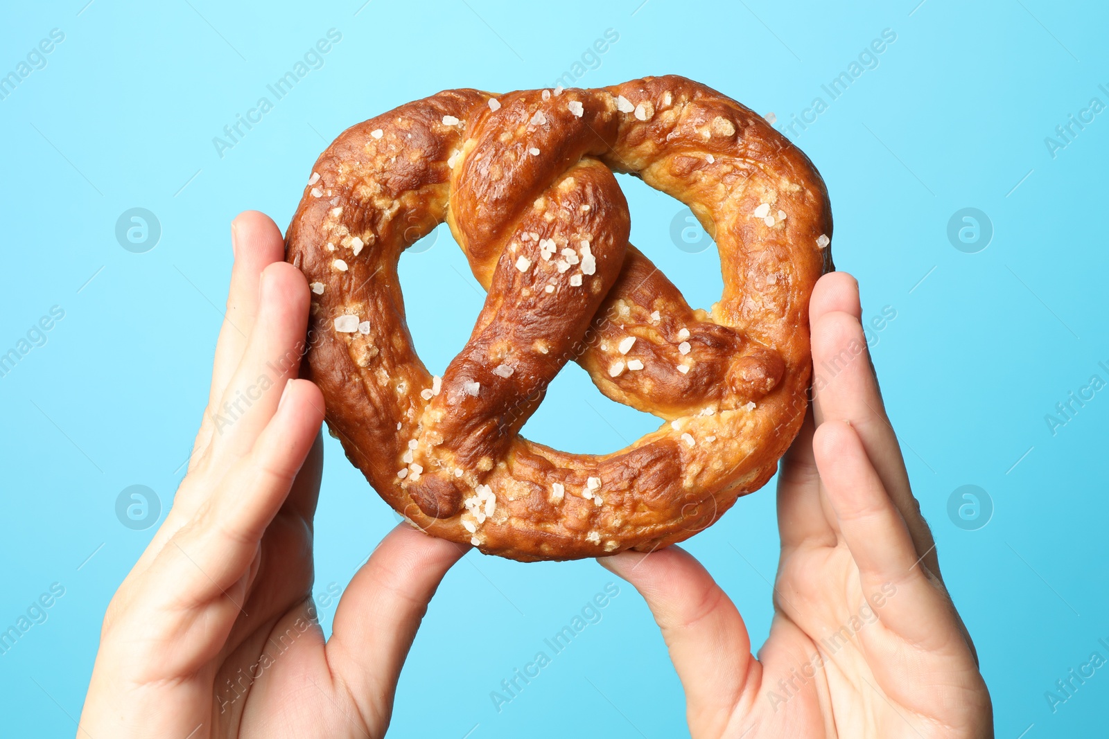 Woman with tasty pretzel on light blue background, closeup Photo of Woman with tasty pretzel on light blue background, closeup