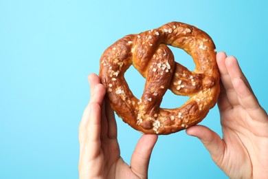 Photo of Woman with tasty pretzel on light blue background, closeup