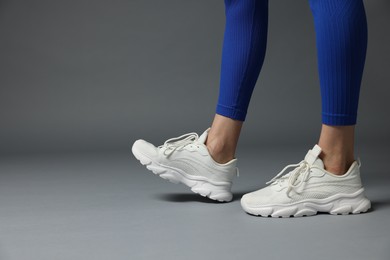 Photo of Woman in white sneakers on gray background, closeup. Space for text