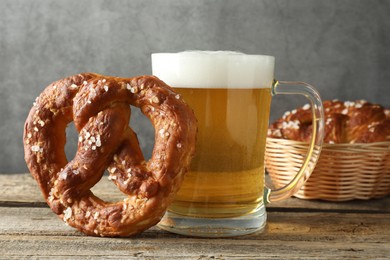 Photo of Tasty pretzel and glass of beer on wooden table against grey background, closeup