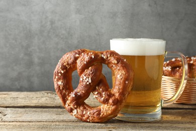 Photo of Tasty pretzel and glass of beer on wooden table against grey background, closeup
