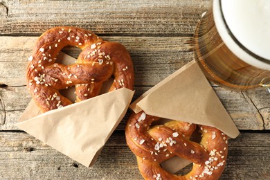 Photo of Tasty pretzels and glass of beer on wooden table, flat lay