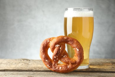 Photo of Tasty pretzel and glass of beer on wooden table against grey background, closeup