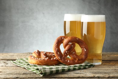 Photo of Tasty pretzels and glasses of beer on wooden table against grey background, closeup