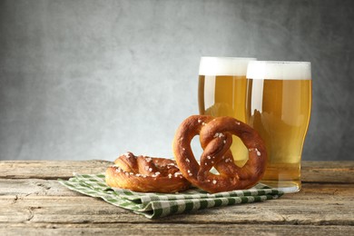 Photo of Tasty pretzels and glasses of beer on wooden table against grey background, closeup