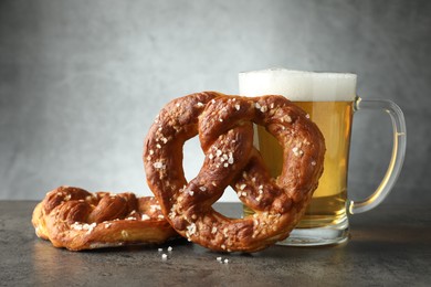 Photo of Tasty pretzels and glass of beer on dark textured table against grey background, closeup