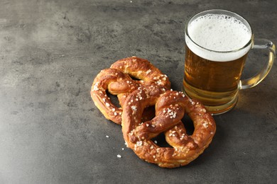 Photo of Tasty pretzels and glass of beer on dark textured table, closeup. Space for text