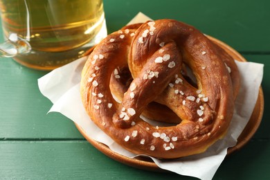 Photo of Tasty pretzels and glass of beer on green wooden table, closeup