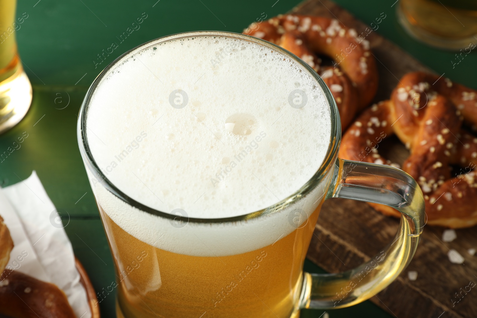 Glass of beer and tasty pretzels on green table, selective focus Photo of Glass of beer and tasty pretzels on green table, selective focus
