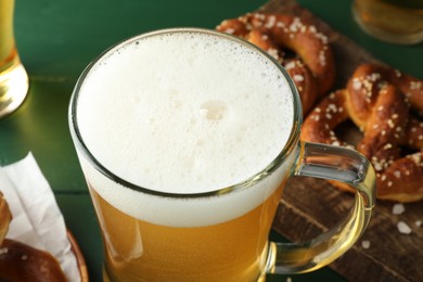 Photo of Glass of beer and tasty pretzels on green table, selective focus