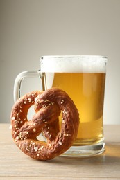 Photo of Tasty pretzel and glass of beer on wooden table against grey background, closeup