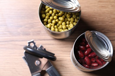 Photo of Can opener and tins with products on wooden table, flat lay