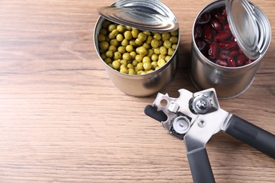 Photo of Can opener and tins with products on wooden table, above view. Space for text