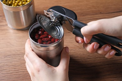 Photo of Woman opening tin of beans with can opener at wooden table, closeup