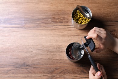 Photo of Woman opening tin of beans with can opener at wooden table, top view. Space for text