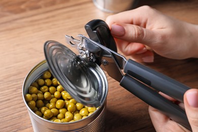 Photo of Woman opening tin of green peas with can opener at wooden table, above view