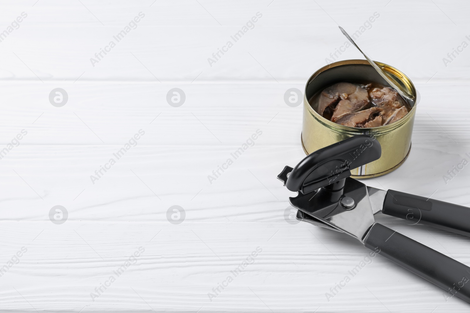 Can opener and tin with fish on white wooden table, closeup. Space for text Photo of Can opener and tin with fish on white wooden table, closeup. Space for text