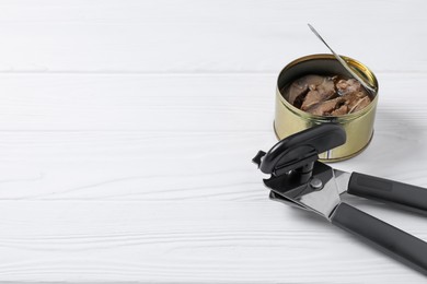 Photo of Can opener and tin with fish on white wooden table, closeup. Space for text