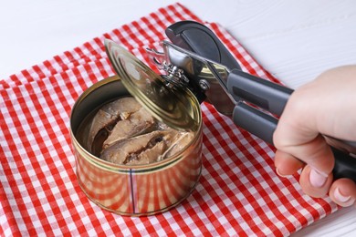 Photo of Woman opening tin of fish with can opener at white wooden table, closeup