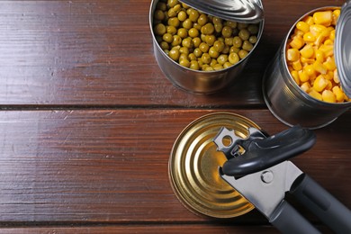 Photo of Can opener and tins with products on wooden table, flat lay. Space for text