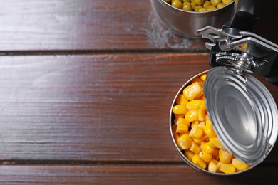 Photo of Can opener and tins with products on wooden table, flat lay. Space for text