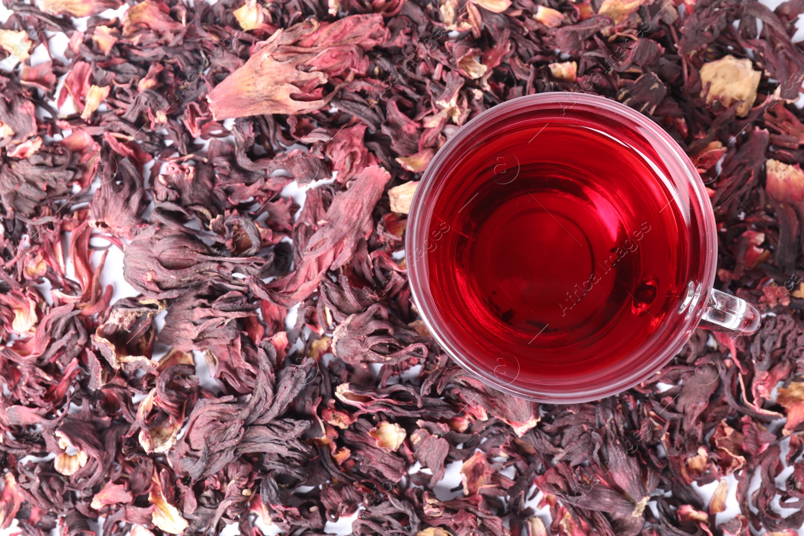 Delicious hibiscus tea in glass cup and dry roselle sepals on table, top view Photo of Delicious hibiscus tea in glass cup and dry roselle sepals on table, top view