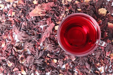 Photo of Delicious hibiscus tea in glass cup and dry roselle sepals on table, top view
