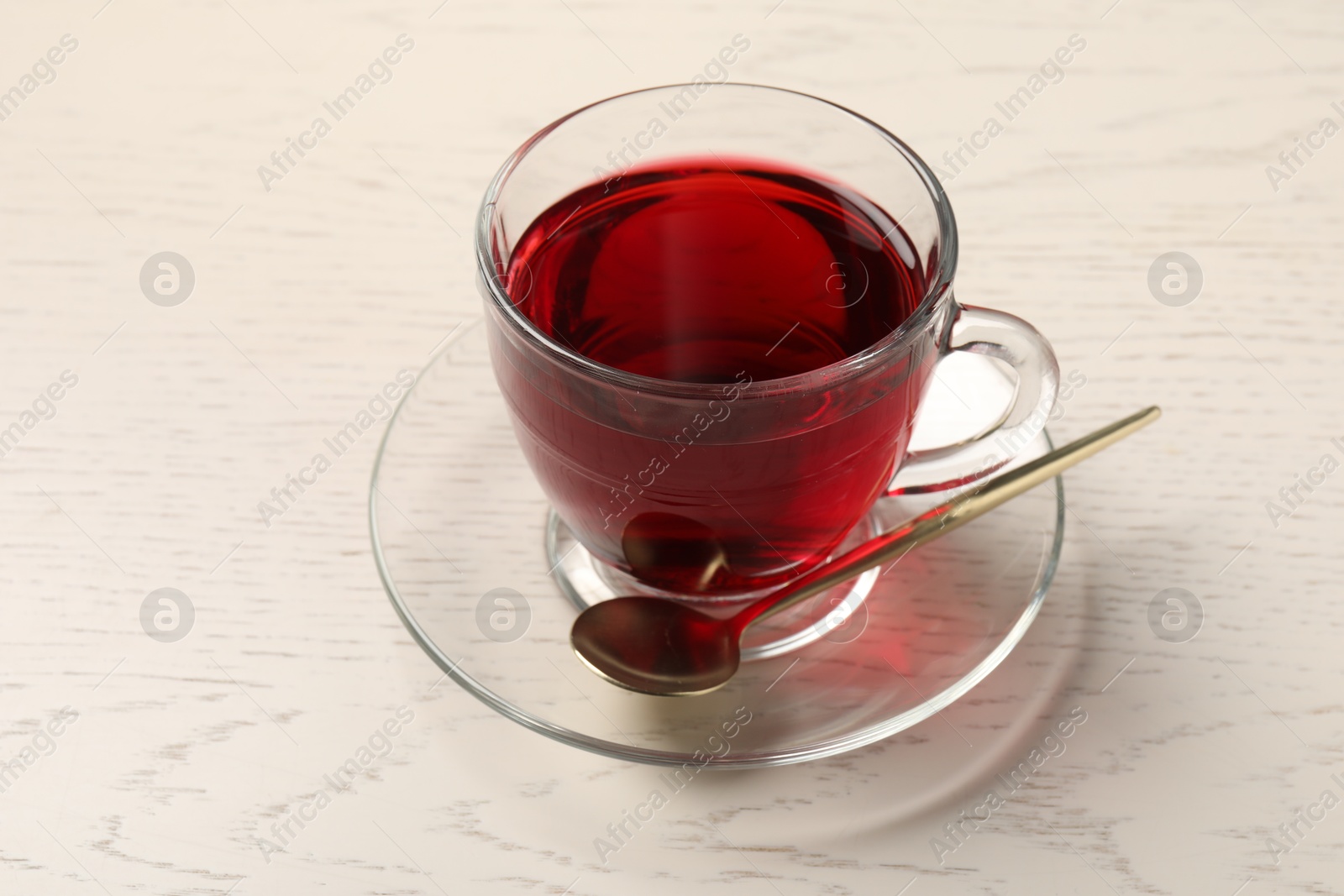 Delicious hibiscus tea in glass cup and spoon on light wooden table, closeup Photo of Delicious hibiscus tea in glass cup and spoon on light wooden table, closeup