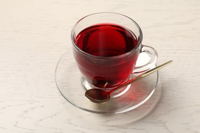 Photo of Delicious hibiscus tea in glass cup and spoon on light wooden table, closeup